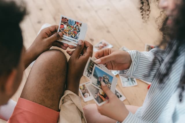 Two people sit looking at colorful printed photographs.